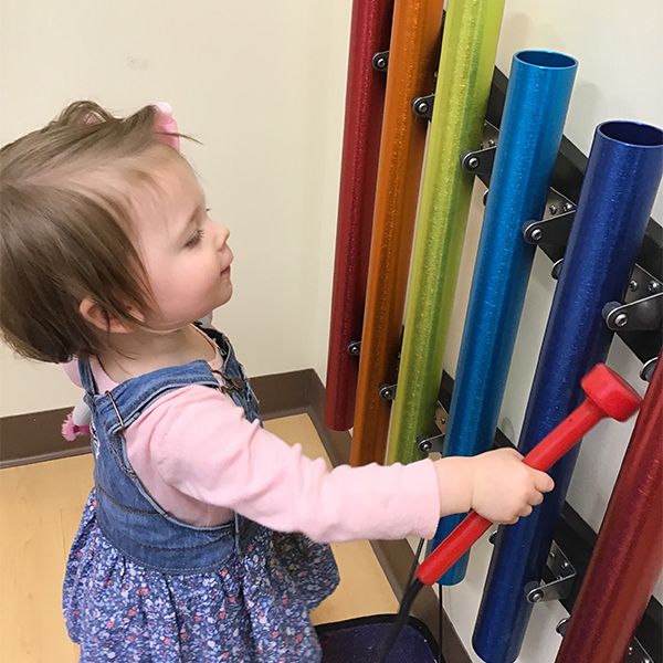 a very young child playing on a wall mounted musical instrument in rainbow colours in their nursery school