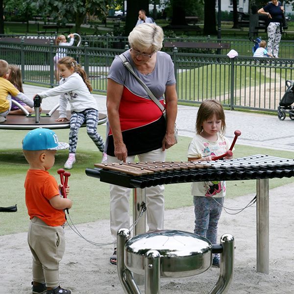 grandmother and two small children playing outdoor musical instruments in a park