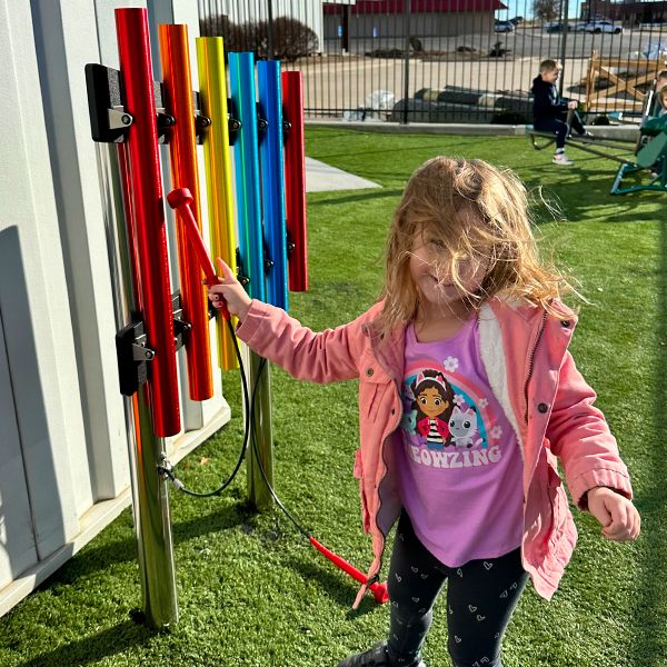 A young boy playing a set of outdoor rainbow chimes in cross church preschool music garden