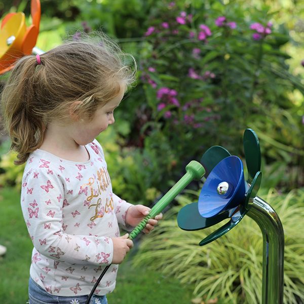 a young girl playing a blue and green musical flower outdoors in a sensory garden