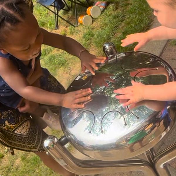 two young children reaching out and playing a large outdoor tongue drum at the Dwight Baldwin Memorial