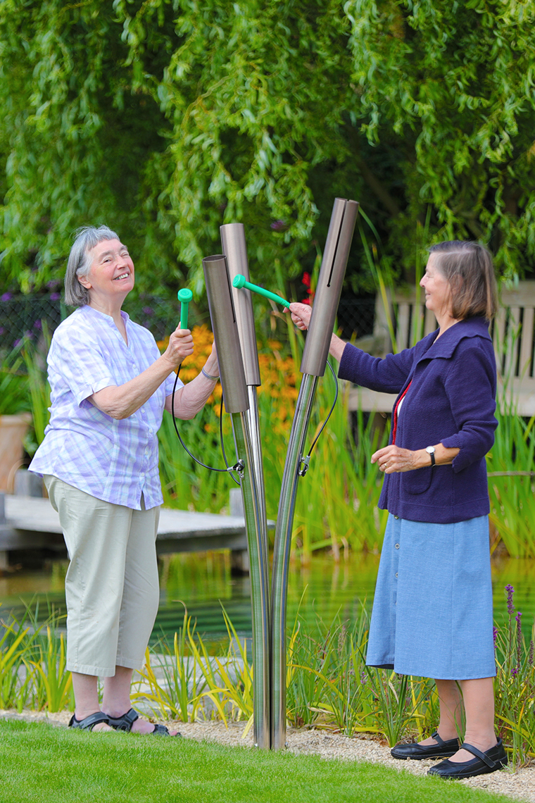 two older ladies playing outdoor musical chimes shaped like cattails