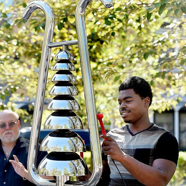 Black man playing a tall silver bell tree in the park