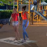 two girls playing on a giant floor piano in a park