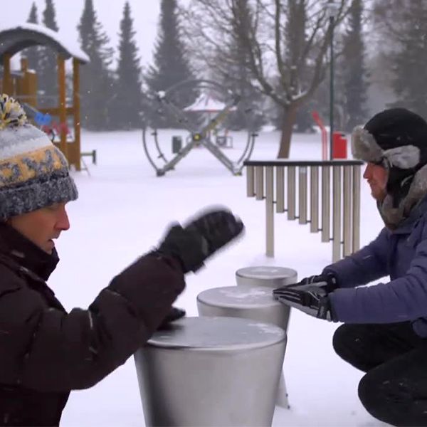 two men playing on metal outdoor drums in a music park in the snow