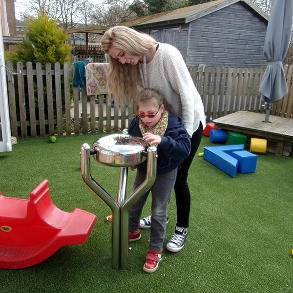 young girl and her carer playing a stainless steel outdoor tongue drum together in special needs school playground