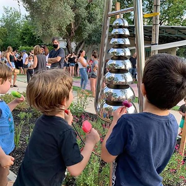 two boys playing a silver musical bell lyre in the Kibbutz Magal musical memorial playground