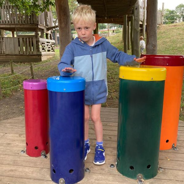 young blond boy playing the outdoor musical drums in rainbow colors at the playground at Bocketts FArm