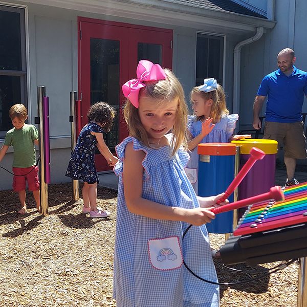 young children playing rainbow colored outdoor musical instruments and chimes in a chruch garden