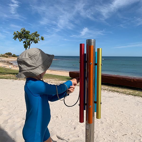 a young boy in swim wear playing a large musical chime post on the beach