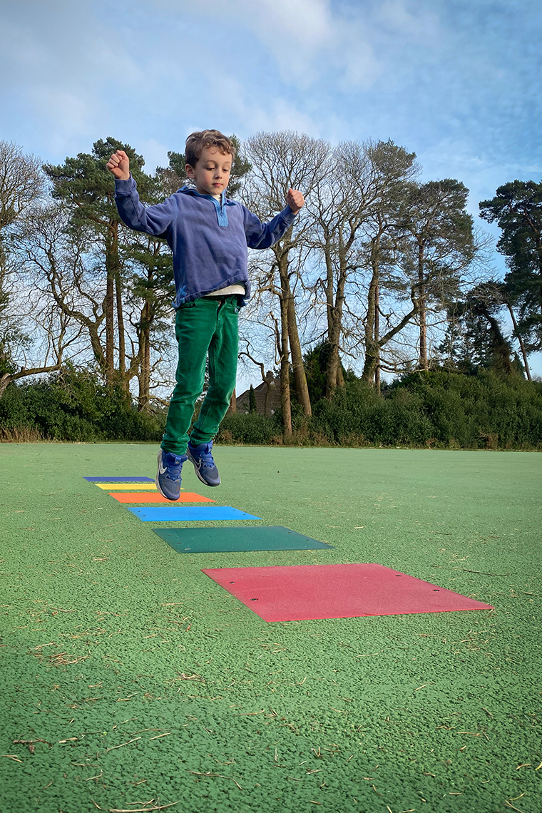 a young boy in a playground jumping onto colored squares that make a musical  tone when activated