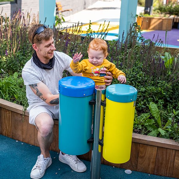 a young red headed girl and her father playing on blue and yellow outdoor conga drums at the Edinburgh Children's Hospital garden
