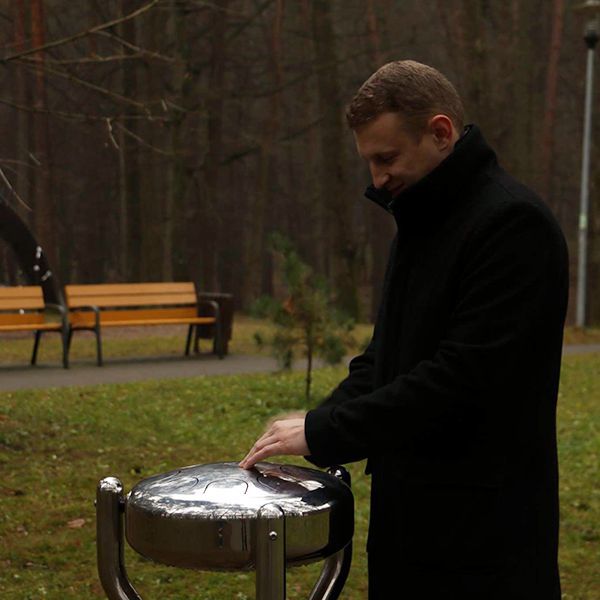 man in a park standing playing a large metal tongue drum