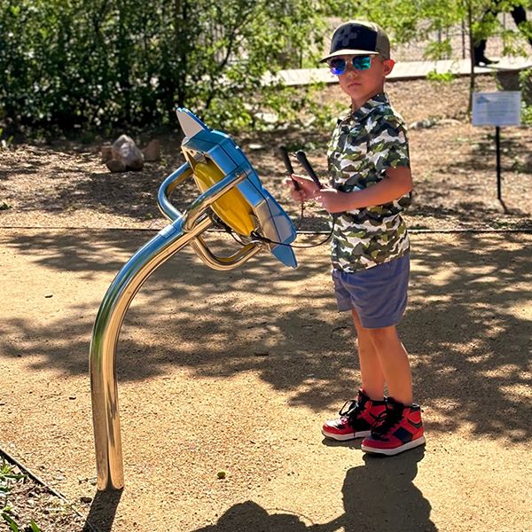 a young boy wearing a hat and sunglasses playing an outdoor musical instrument shaped like a flower with a tongue drum center