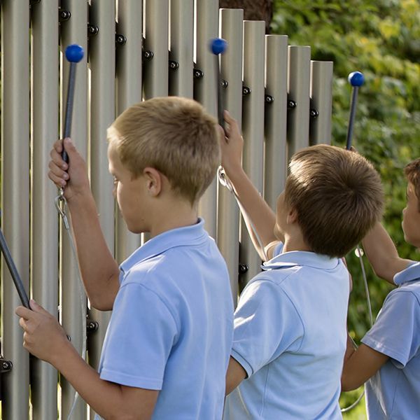 Three schoolboys in uniform playing musical chimes with blue beaters in a playground