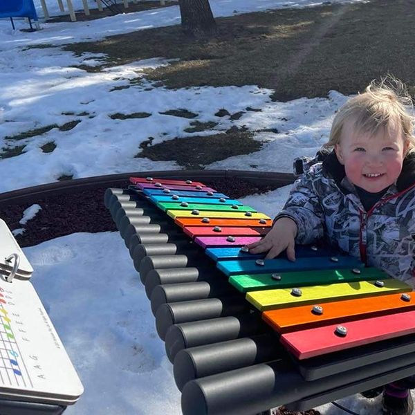 small child in the snow playing a rainbow colored outdoor xylophone