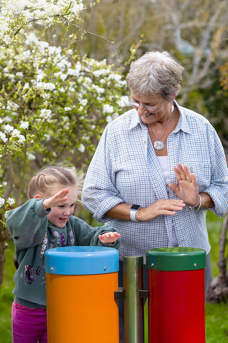 a young girl and her grandmother playing outdoor musical drums with a tree in blossom behind