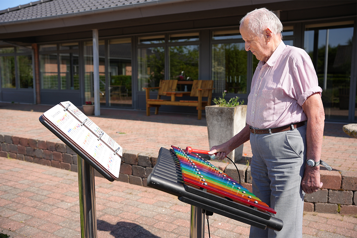 senior male playing a rainbow coloured outdoor xylophone in a care home garden