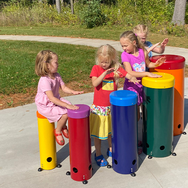 four young girls playing on large colorful outdoor drums in a musical playground in a park