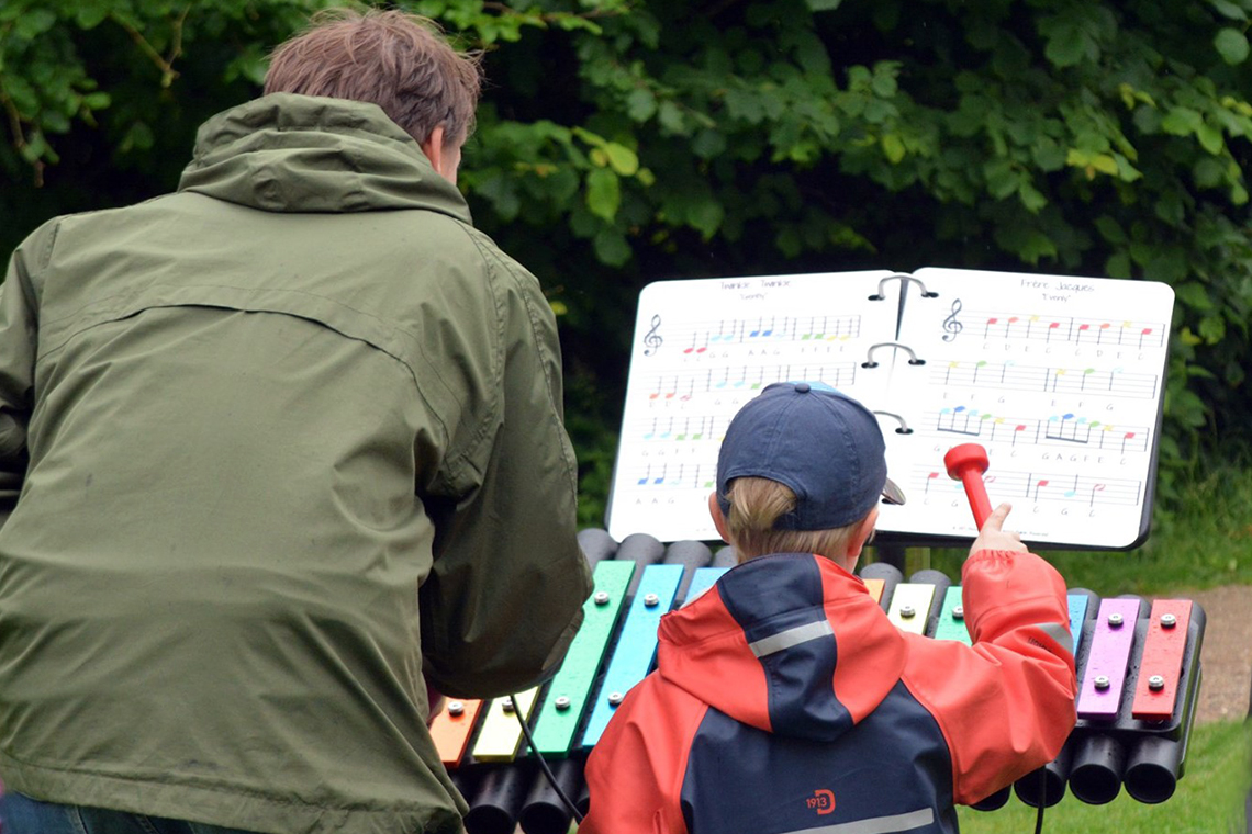 A father and son playing an outdoor xylophone with an outdoor music book