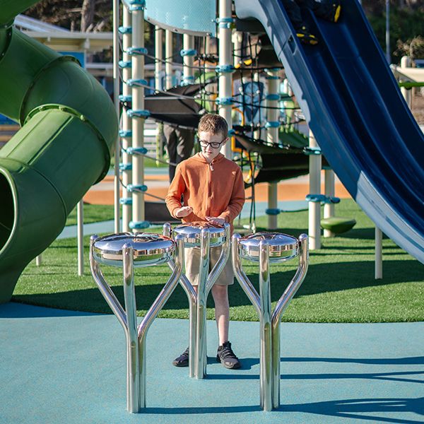 a boy playing a stainless steel tongue drum with a large slide behind him in McLaren Park