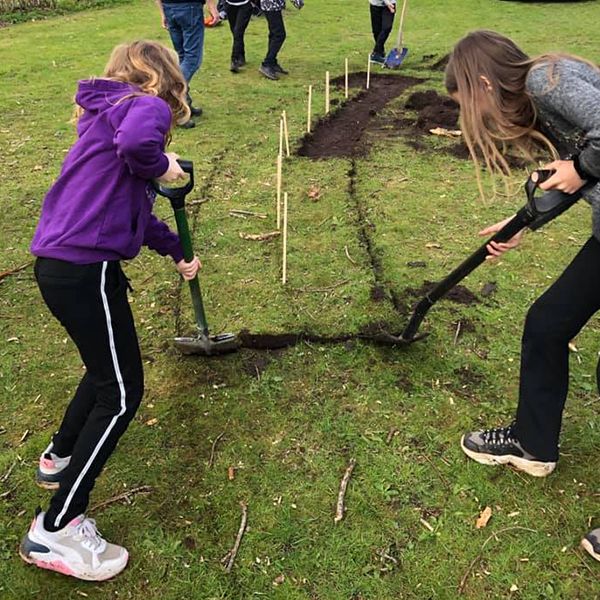 two schoolchildren removing the turf in their playground ready for a new outdoor musical instrument