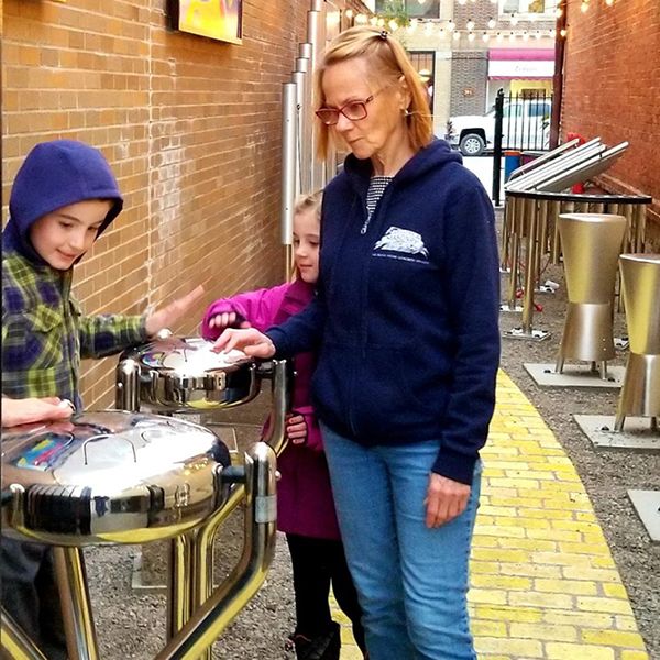 Young broher and sister playing a stainless steel outdoor tongue drum in the new Go Art! Play Me A Tune Music Garden