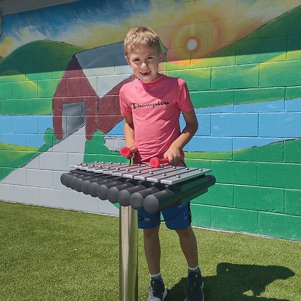 a young boy playing an outdoor xylophone with red mallets at the musical garden in town of versailles