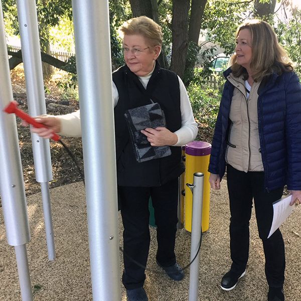 two ladies playing tall silver tubular Bell chimes in the aldeburgh hospital sensory garden