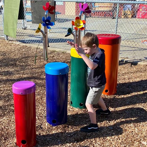 Young boy playing on colorful outdoor musical drums in his school playground