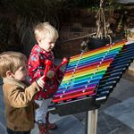 two little boys playing a large rainbow coloured xylophone in a playground