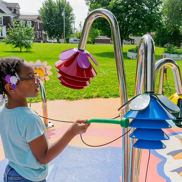 young african american girl playing outdoor musical chimes shaped like flowers in a music park