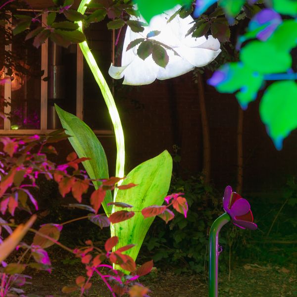 outdoor musical flower bell alongside a large flower sculpture in a sculpture park at night lit in white light