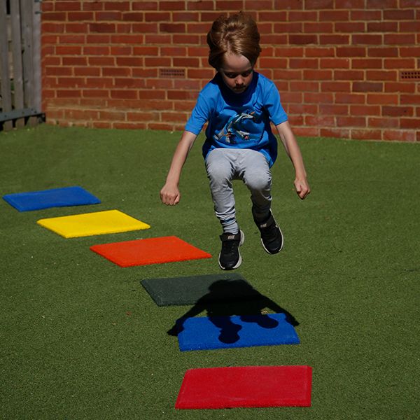 a young boy jumping on a set of six multicolored square 'pads' with hidden bells beneath them