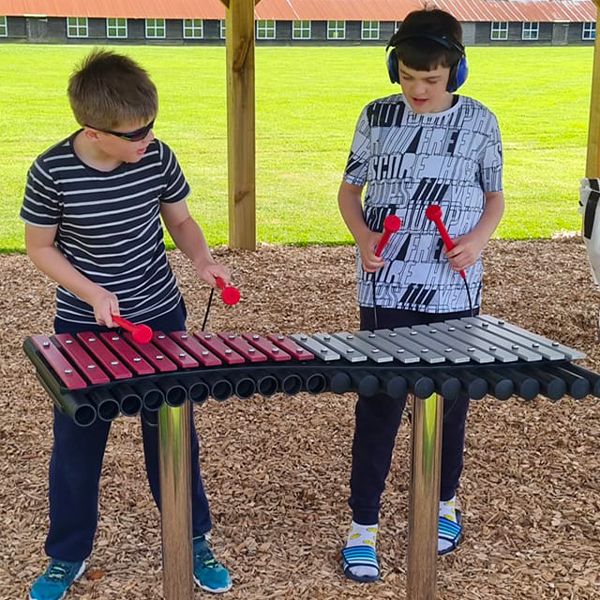 Two children playing an outdoor xylophone with pink and silver notes at the Thomas Centre music pavilion