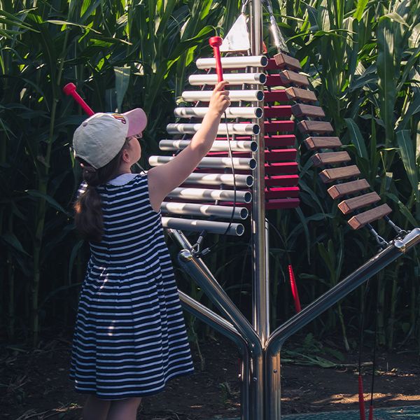 Young girl playing a large outdoor musical instrument with three sets of notes descending from a central post