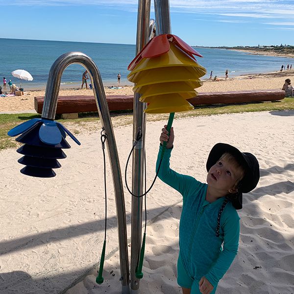 a young boy in swim wear playing a large outdoor musical instrument shaped like flowers on the beach