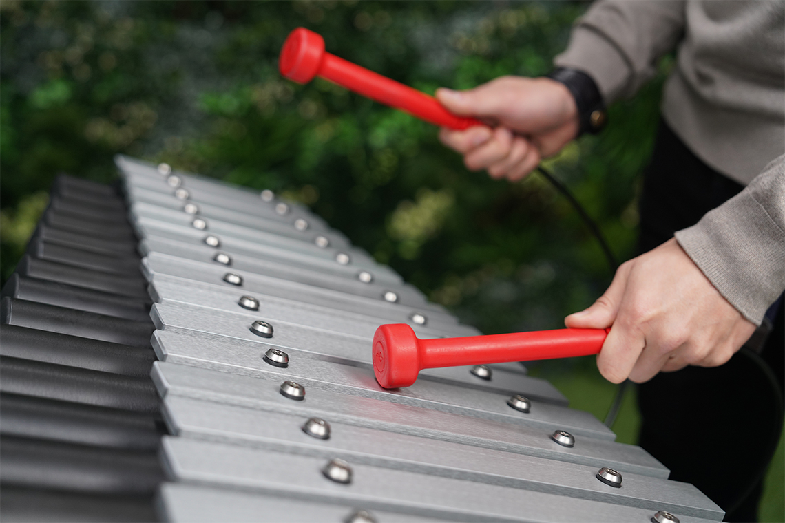 close up image of an outdoor xylophone being played with red mallets