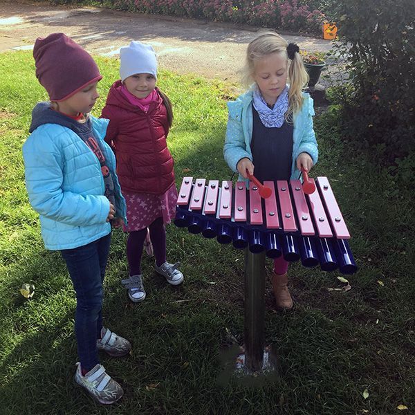 Three little girls playing a large outdoor xylophone with pink notes in a playground