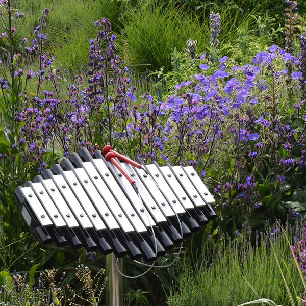 an outdoor musical instrument like a xylophone with flowers behind in a sensory garden