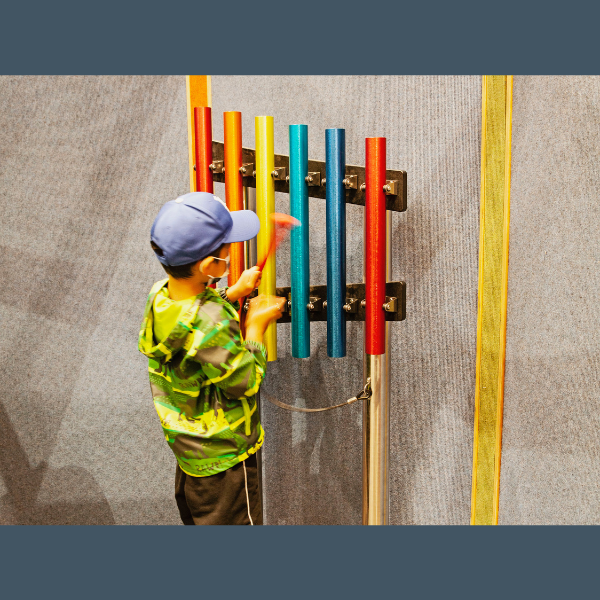 a little boy playing rainbow colored chimes on a wall inside the palo alto zoo