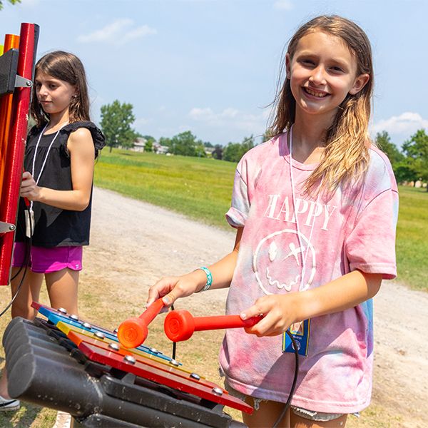 young teenage girl wearing a pink t shirt playing an outdoor xylophone with rainbow colored notes