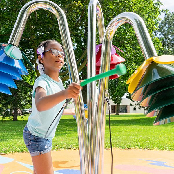 a young african american girl playing outdoor musical chimes shaped like flowers in a music park