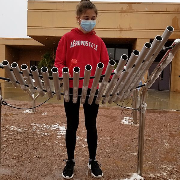 A schoolgirl wearing a red uniform playing an outdoor musical instrument in the school playground