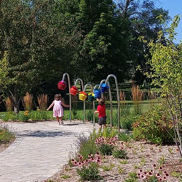 two small children playing on a row of outdoor musical instruments shaped like flowers outside Benzies Shore Library