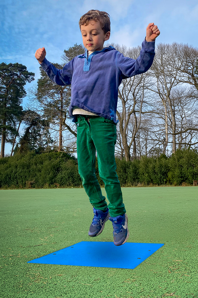 Young boy in a playground jumping onto a square blue outdoor musical chime 