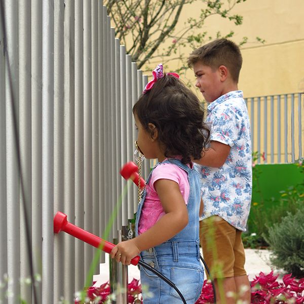 a young girl and taller boy playing a set of large outdoor musical chimes in a music park or playground