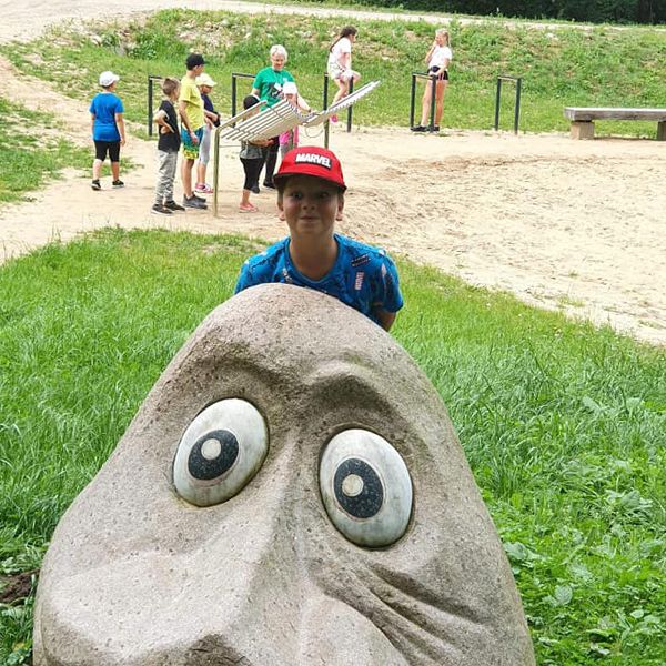 stone character at Sirvetos Regional Park Lithuania with children playing an outdoor musical instrument in the background