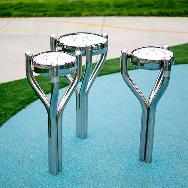 three outdoor stainless steel tongue drums on a blue playground surface