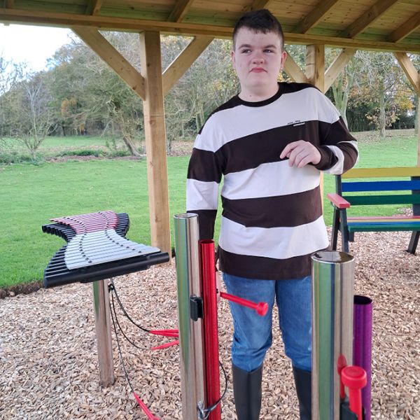 A young man with autism enjoying a playful moment on colorful outdoor musical chimes at the Thomas Centre